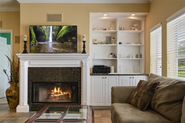 living room with ornamental molding, built in features, and a high end fireplace