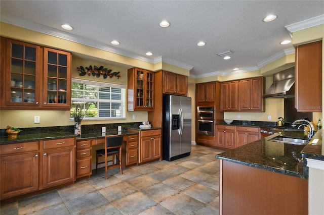 kitchen with built in desk, sink, dark stone counters, stainless steel appliances, and wall chimney range hood