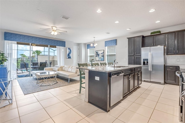 kitchen featuring a center island with sink, sink, light stone countertops, appliances with stainless steel finishes, and decorative light fixtures