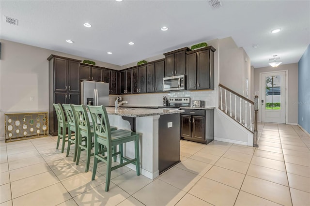 kitchen featuring a kitchen island with sink, a kitchen breakfast bar, appliances with stainless steel finishes, and dark brown cabinets