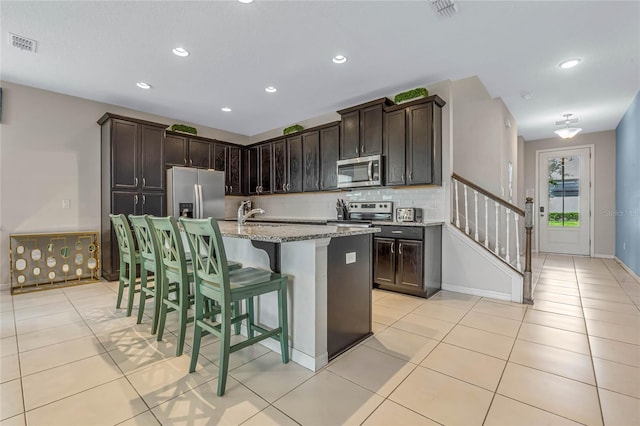 kitchen featuring a center island with sink, light stone countertops, visible vents, and stainless steel appliances