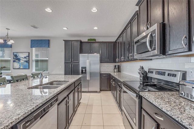 kitchen with stainless steel appliances, light tile patterned floors, light stone countertops, hanging light fixtures, and sink