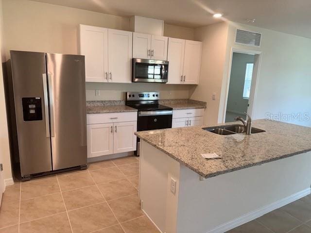 kitchen featuring white cabinetry, sink, light stone counters, light tile patterned floors, and appliances with stainless steel finishes