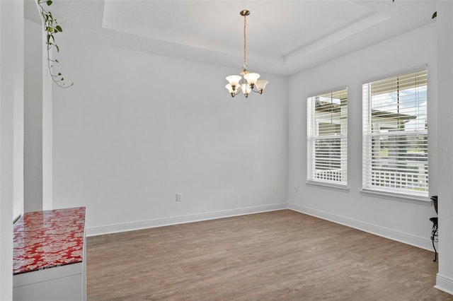 empty room with a notable chandelier, hardwood / wood-style flooring, and a raised ceiling