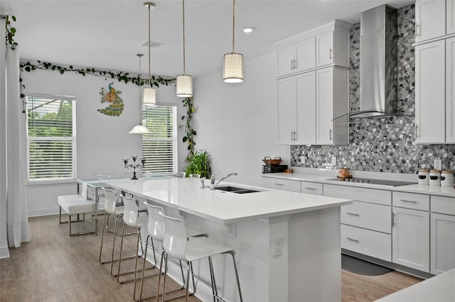 kitchen with sink, a kitchen island with sink, black electric stovetop, and wall chimney range hood