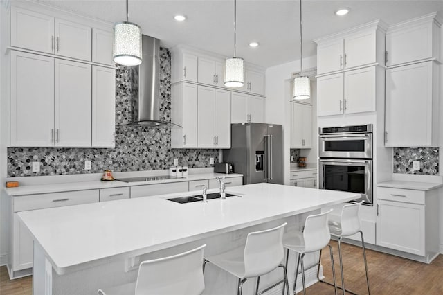 kitchen with white cabinetry, wall chimney range hood, and an island with sink