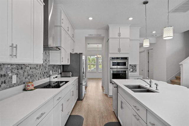 kitchen with sink, white cabinets, pendant lighting, and wall chimney exhaust hood