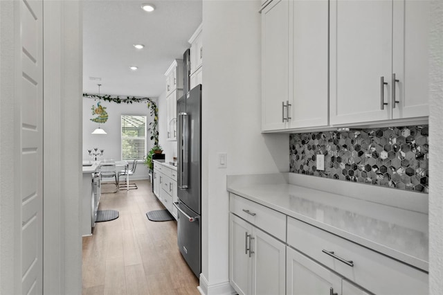 kitchen featuring white cabinets, tasteful backsplash, high quality fridge, and light hardwood / wood-style floors