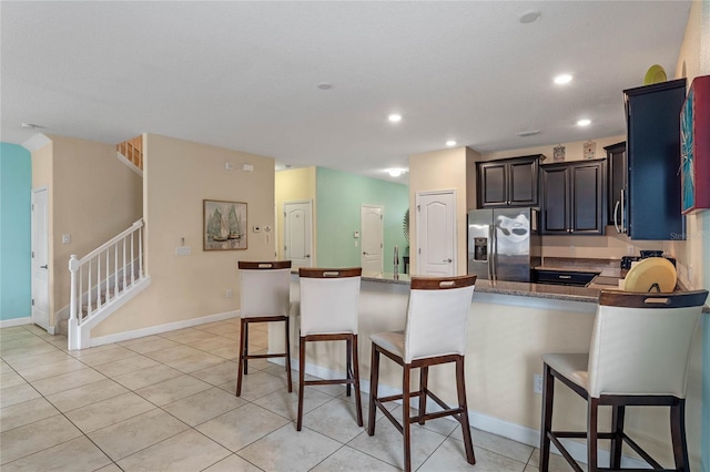 kitchen featuring light tile patterned floors, a breakfast bar, stainless steel fridge, and kitchen peninsula