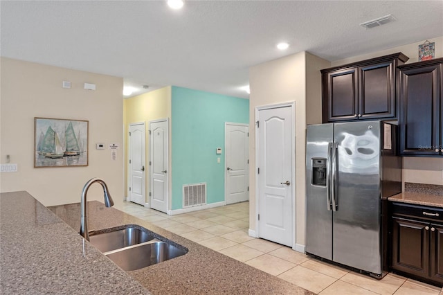 kitchen featuring dark brown cabinetry, stainless steel refrigerator with ice dispenser, sink, light tile patterned floors, and stone counters