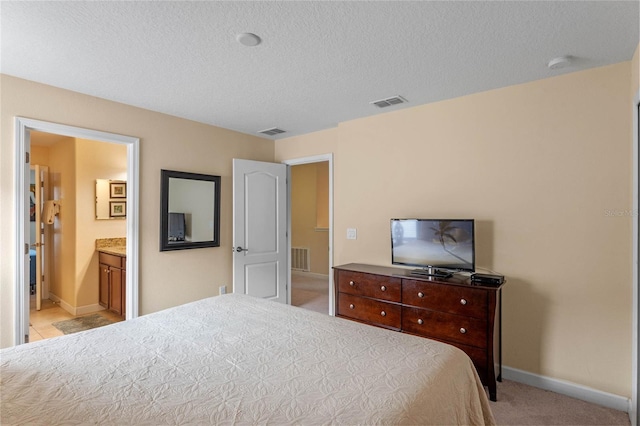 bedroom with a textured ceiling, ensuite bathroom, and light carpet