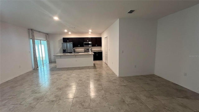 kitchen with dark brown cabinets, light tile patterned floors, stainless steel appliances, sink, and a center island with sink