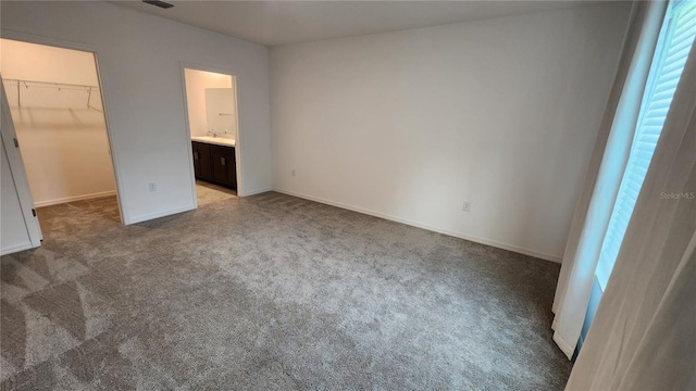 unfurnished bedroom with ensuite bath, a spacious closet, light colored carpet, and a closet