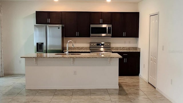 kitchen with light tile patterned floors, appliances with stainless steel finishes, light stone counters, and a center island with sink