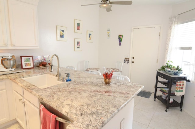 kitchen with light stone counters, sink, kitchen peninsula, light tile patterned flooring, and ceiling fan