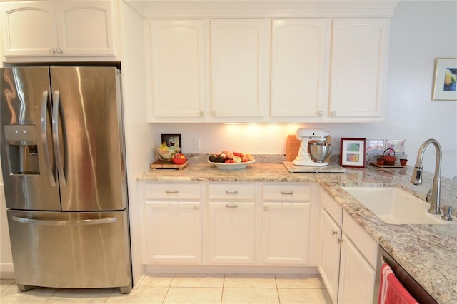 kitchen with stainless steel fridge, white cabinetry, light tile patterned floors, light stone counters, and sink