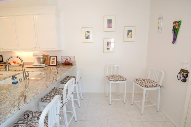 kitchen featuring light tile patterned floors, sink, light stone countertops, and white cabinets