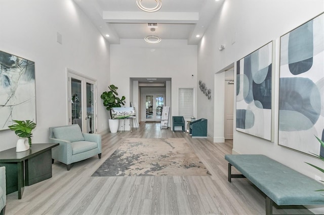 corridor featuring beamed ceiling, french doors, light hardwood / wood-style floors, and a high ceiling