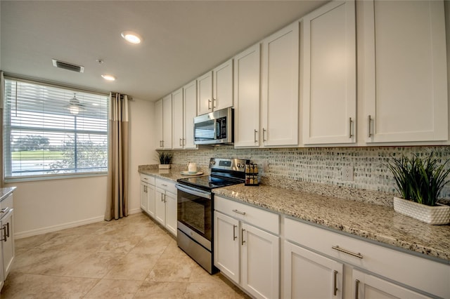 kitchen with light stone countertops, light tile patterned floors, tasteful backsplash, white cabinets, and appliances with stainless steel finishes