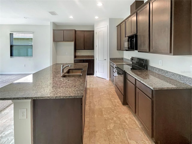 kitchen featuring sink, dark stone counters, dark brown cabinetry, a center island with sink, and black appliances