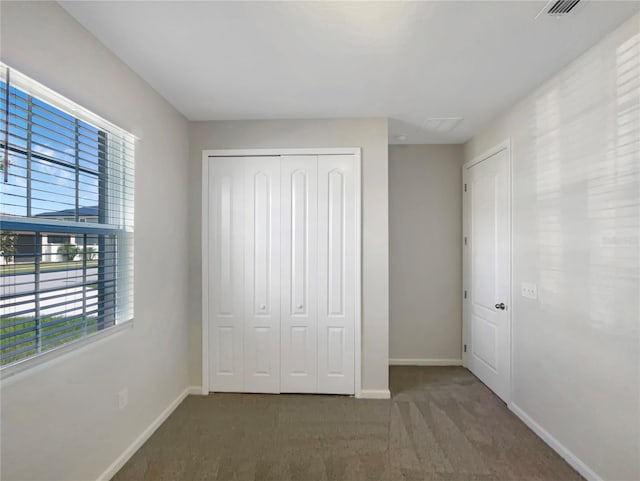 unfurnished bedroom with a closet, multiple windows, and dark colored carpet