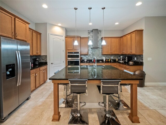 kitchen with a breakfast bar, pendant lighting, a kitchen island with sink, stainless steel appliances, and wall chimney range hood