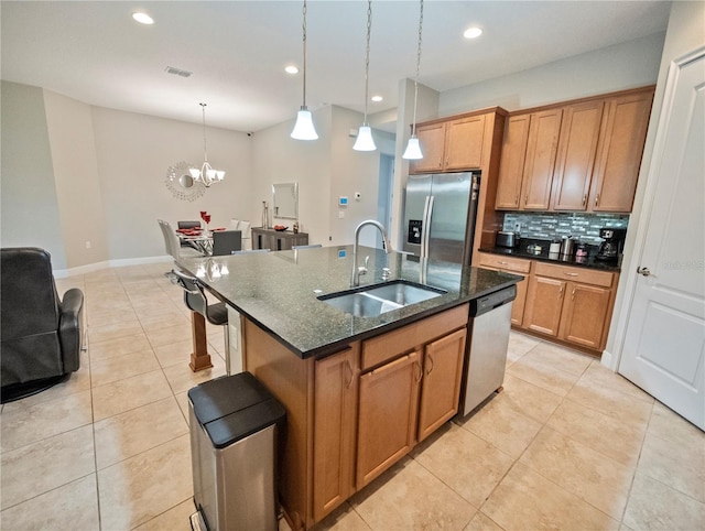 kitchen featuring sink, appliances with stainless steel finishes, an island with sink, pendant lighting, and dark stone counters