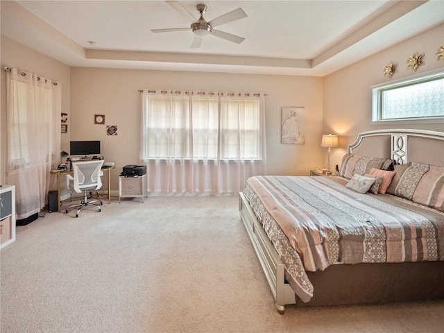 bedroom with ceiling fan, a tray ceiling, and light carpet