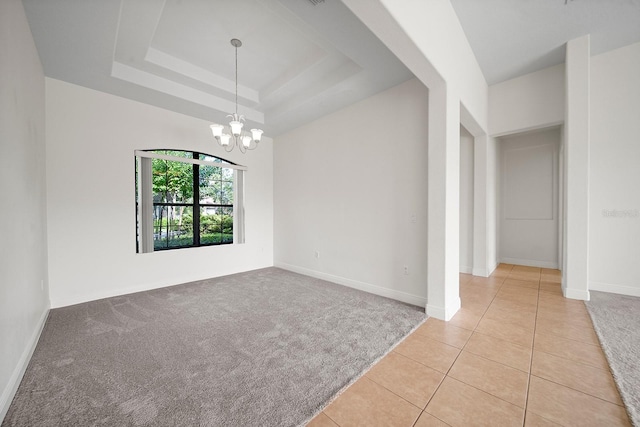 tiled spare room featuring a raised ceiling and a chandelier