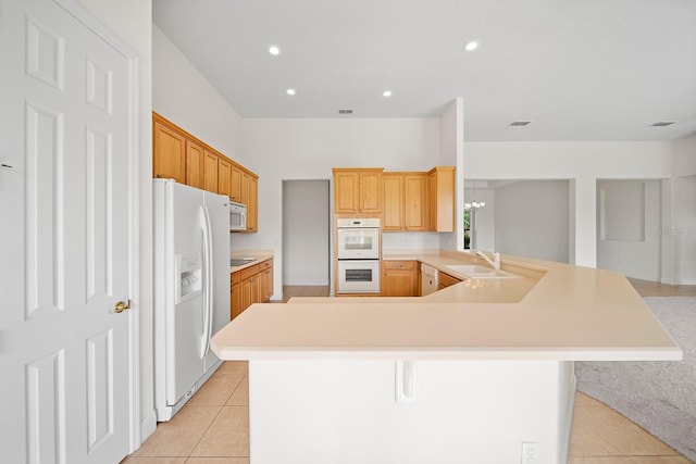 kitchen featuring sink, white appliances, a kitchen breakfast bar, light tile patterned floors, and kitchen peninsula