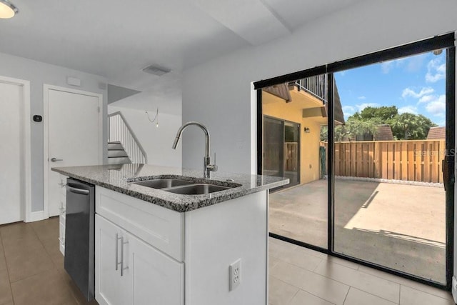 kitchen with sink, white cabinetry, dark stone countertops, stainless steel dishwasher, and an island with sink