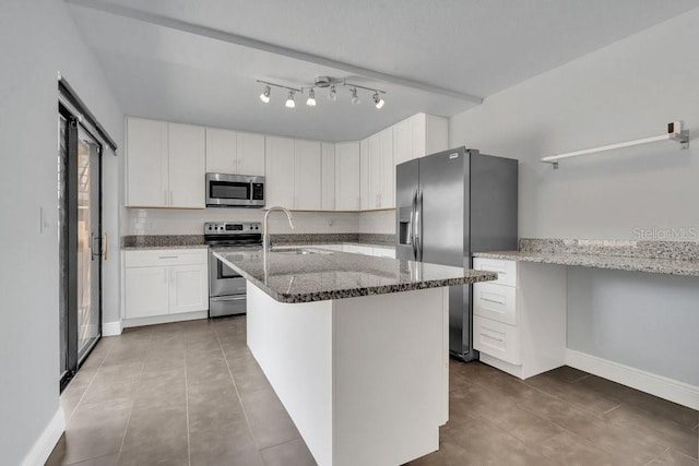 kitchen featuring appliances with stainless steel finishes, sink, white cabinets, light stone counters, and a center island with sink