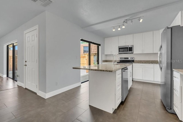 kitchen featuring dark tile patterned floors, a kitchen island with sink, white cabinetry, stainless steel appliances, and light stone counters