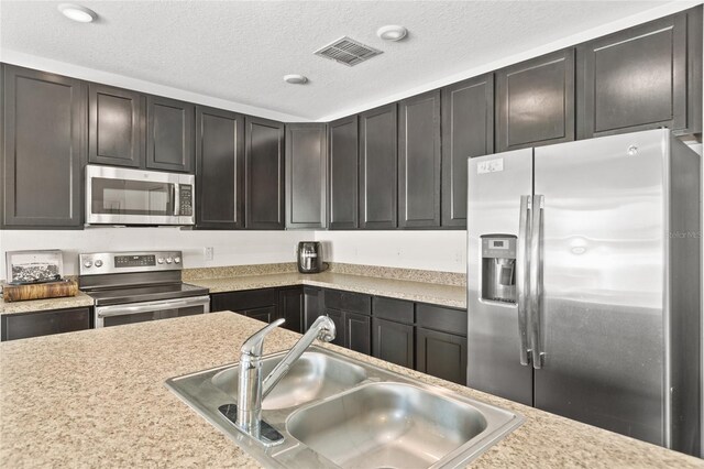 kitchen featuring stainless steel appliances, dark brown cabinets, sink, and a textured ceiling