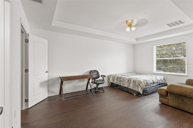 bedroom with dark wood-type flooring, ceiling fan, and a raised ceiling