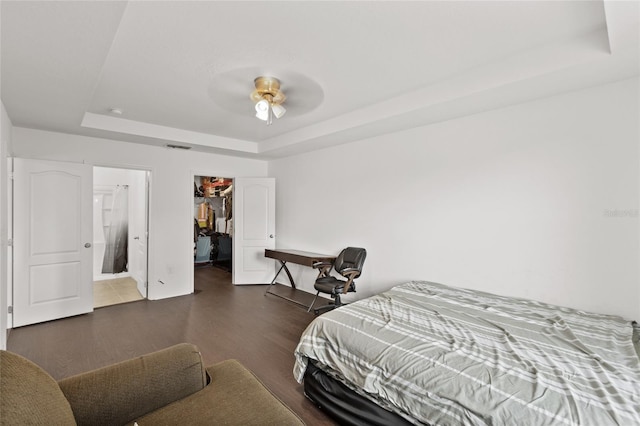 bedroom featuring a walk in closet, dark hardwood / wood-style floors, a raised ceiling, a closet, and ceiling fan