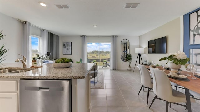 kitchen featuring light tile patterned floors, light stone counters, a wealth of natural light, and stainless steel dishwasher