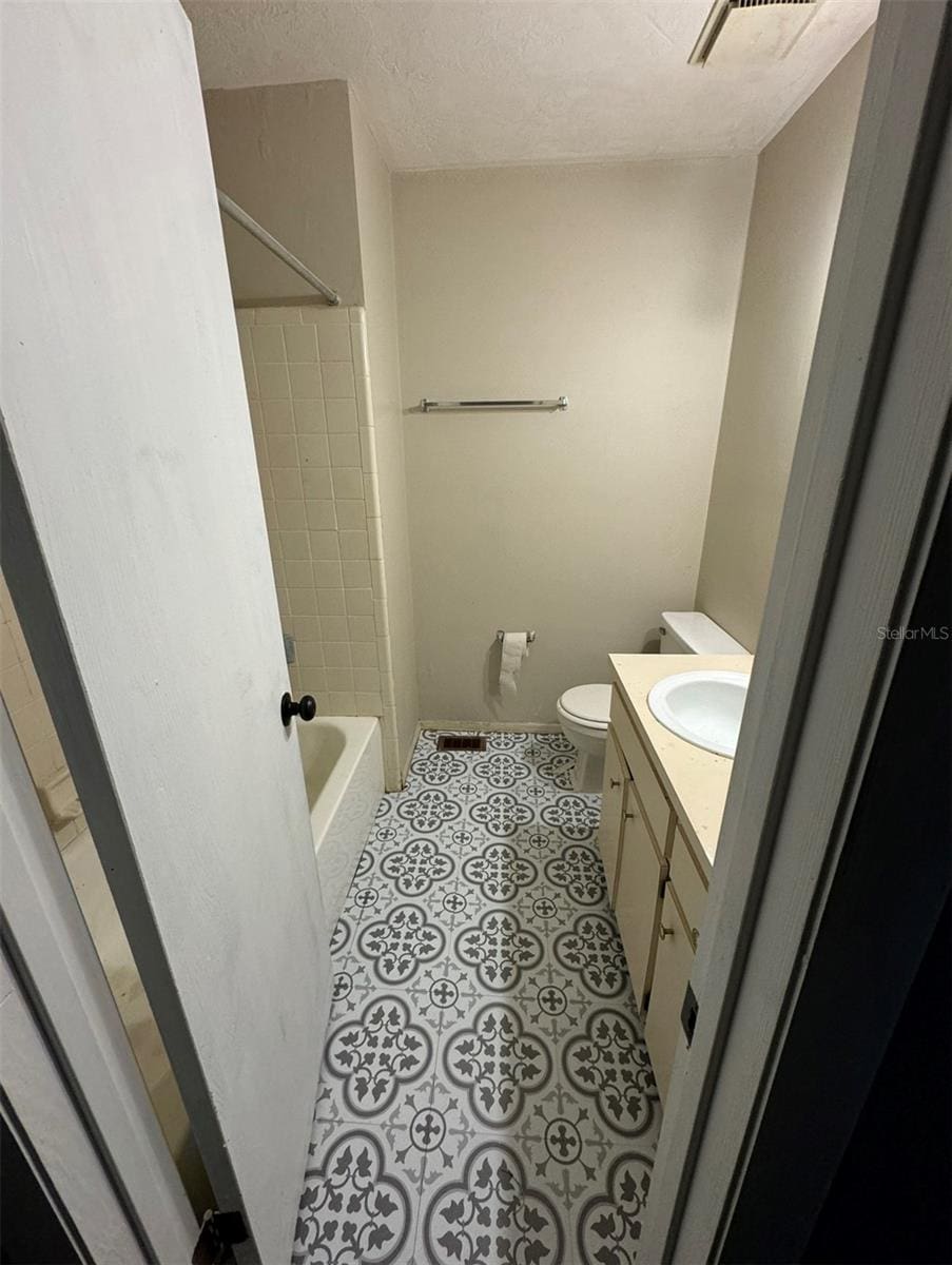 full bathroom featuring vanity, toilet, a textured ceiling, and tiled shower / bath combo