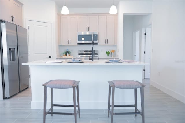 kitchen featuring hanging light fixtures, appliances with stainless steel finishes, a kitchen island with sink, and a kitchen breakfast bar