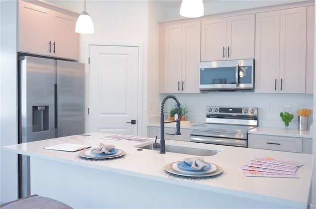 kitchen featuring stainless steel appliances, sink, hanging light fixtures, and a center island with sink