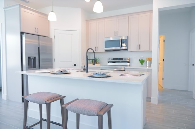 kitchen featuring a kitchen bar, hanging light fixtures, a center island with sink, appliances with stainless steel finishes, and white cabinets