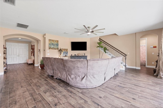 living room featuring arched walkways, visible vents, stairs, and wood finished floors