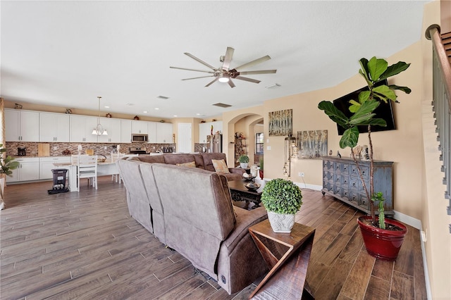 living room with a ceiling fan, wood finished floors, arched walkways, and baseboards