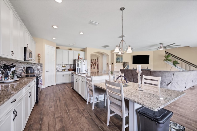 kitchen featuring dark wood finished floors, a kitchen bar, arched walkways, and appliances with stainless steel finishes