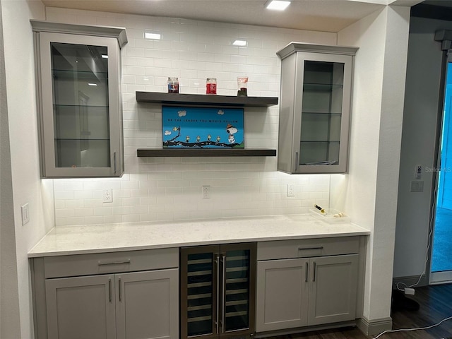 bar featuring tasteful backsplash, light stone countertops, dark wood-type flooring, gray cabinets, and beverage cooler