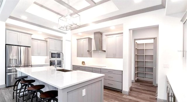 kitchen featuring appliances with stainless steel finishes, decorative light fixtures, a kitchen island with sink, wall chimney range hood, and hardwood / wood-style flooring