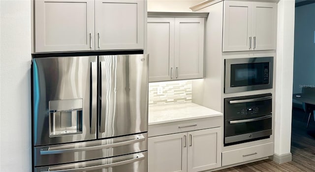 kitchen with backsplash, stainless steel appliances, white cabinetry, dark hardwood / wood-style floors, and light stone countertops