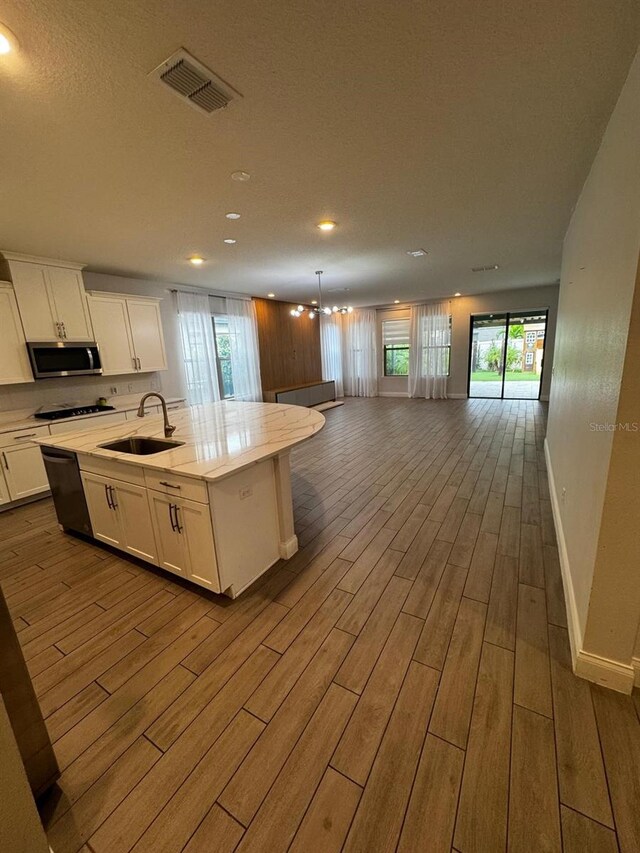 kitchen with sink, white cabinetry, a kitchen island with sink, light hardwood / wood-style floors, and decorative light fixtures