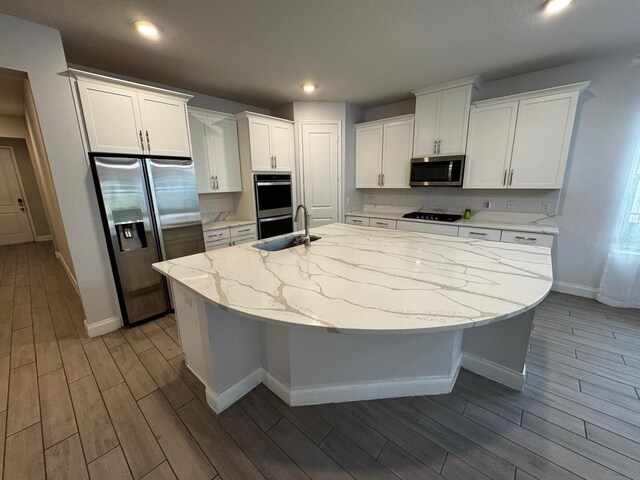 kitchen featuring stainless steel appliances, white cabinetry, an island with sink, and light stone counters