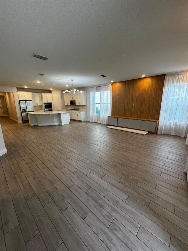 unfurnished living room with a textured ceiling, light wood-type flooring, and wood walls